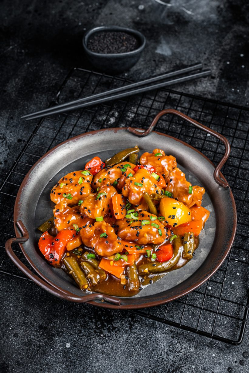 Chicken meat in sweet and sour sauce in a steel tray. Black background. Top view.